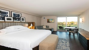 Quarto de hotel com uma cama grande, um sofá, uma mesinha e uma varanda com vista.