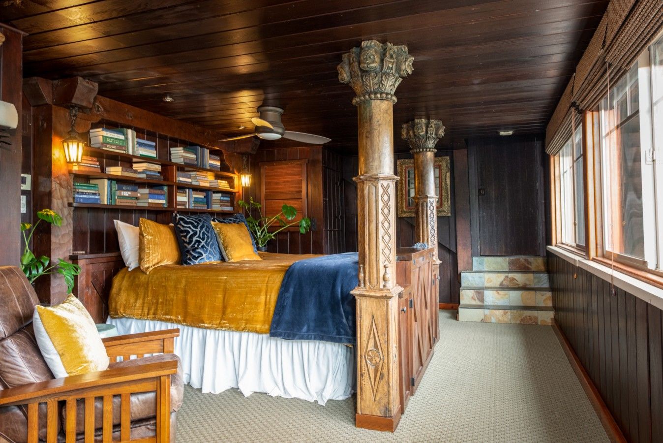 A room with a bed, wooden columns, a bookshelf, and a window.