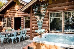 A log cabin with a hot tub, outdoor seating, and a window overlooking a waterfall.