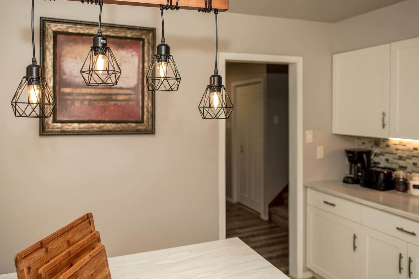 Une cuisine avec des meubles blancs, une table en bois et un tableau encadré accroché au mur.