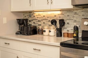 Una cocina con cafetera, tarros de azúcar y café en polvo, un recipiente de aceite y un tostador.