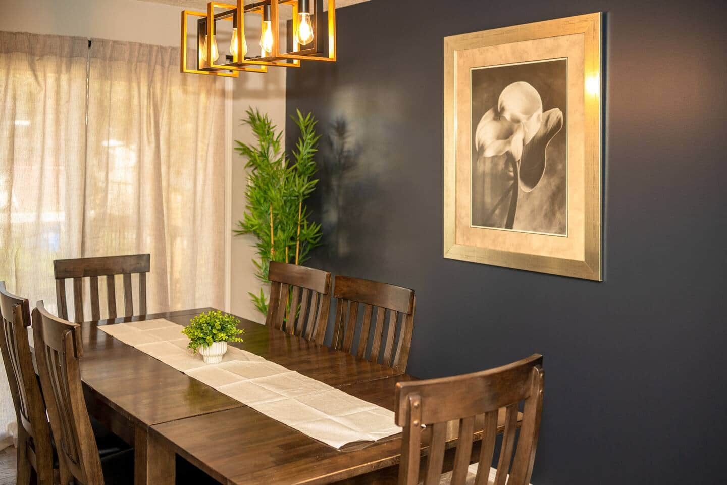Un coin repas avec une table en bois, des chaises, un vase contenant des plantes vertes et un tableau encadré au mur.