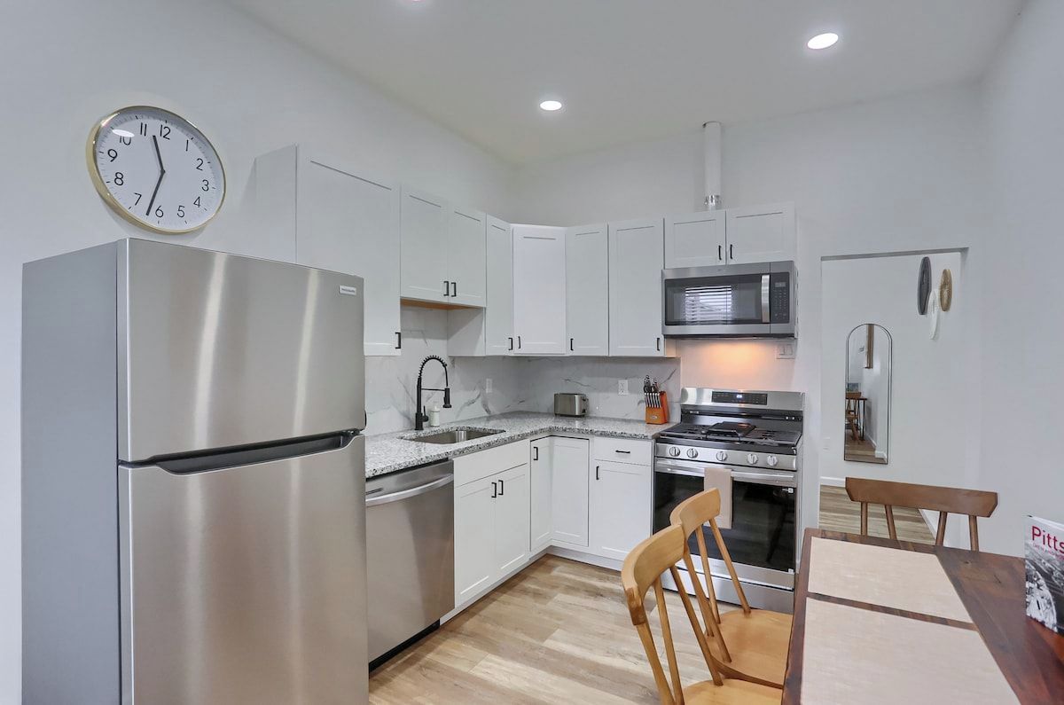 Una cocina moderna con electrodomésticos de acero inoxidable, muebles blancos y una mesa de comedor de madera.