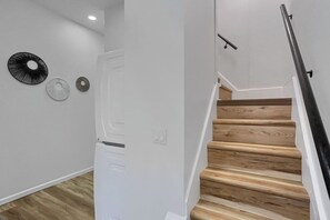 Una escala de fusta amb barana negra que condueix a una porta blanca amb mànec rodó.