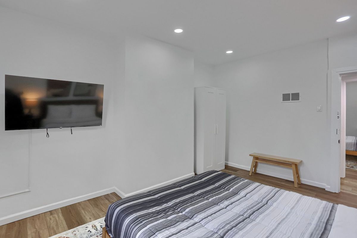 Ein Schlafzimmer mit einem Bett, einem an der Wand befestigten Fernseher, einem Kleiderschrank und einer Bank.
