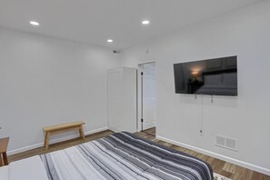 Un dormitorio con cama, un banco, un armario, un televisor montado en la pared y luces empotradas en el techo.
