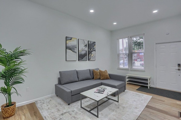 A modern living room with a grey sofa, a coffee table, and a potted plant. - Carnegie, W Main St 208 A Cozy 2 Bedroom Private Apartment (Carnegie)