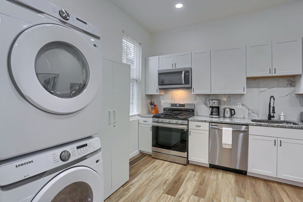 Een moderne keuken met witte kasten, een magnetron, fornuis, oven en vaatwasser.