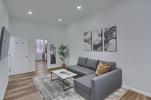 A modern living room with a grey sofa, a coffee table, and a large mirror. There are abstract paintings on the wall and a potted plant. - Carnegie, W Main St 208 A Cozy 2 Bedroom Private Apartment (Carnegie)