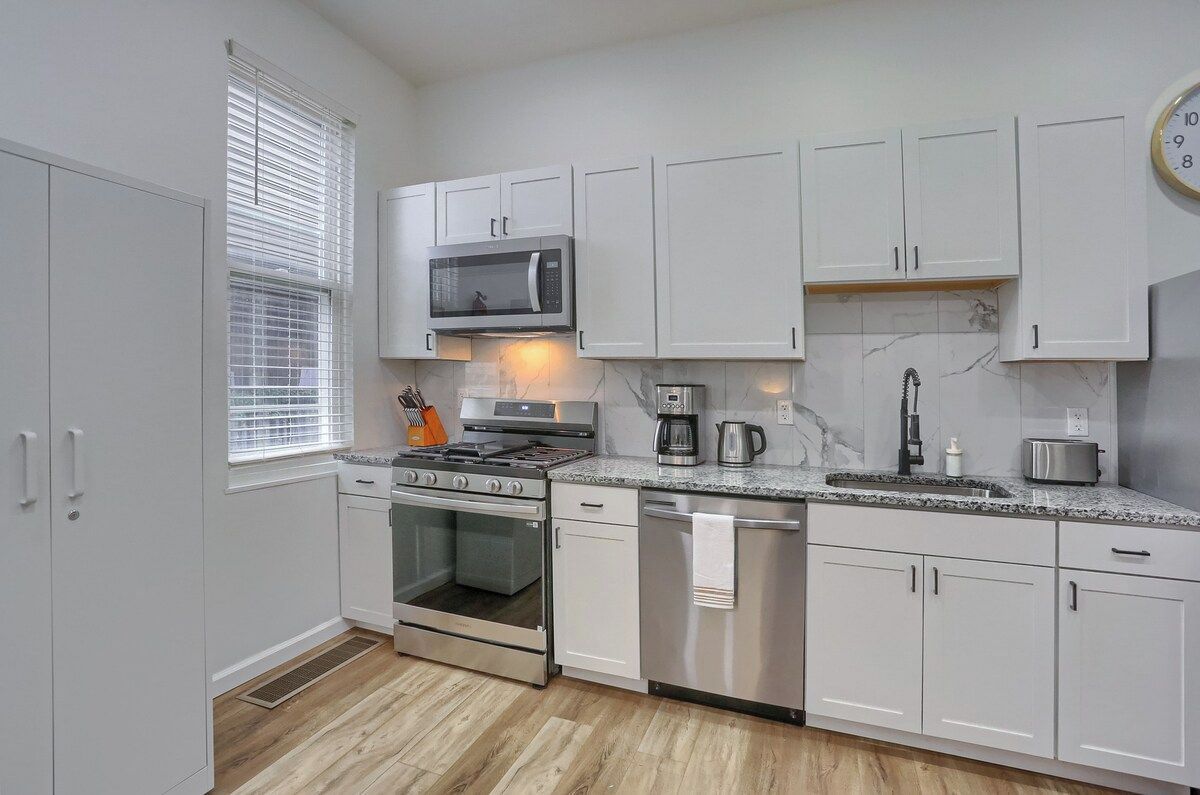 A modern kitchen with white cabinets, a microwave, stove, coffee maker, and a dishwasher.
