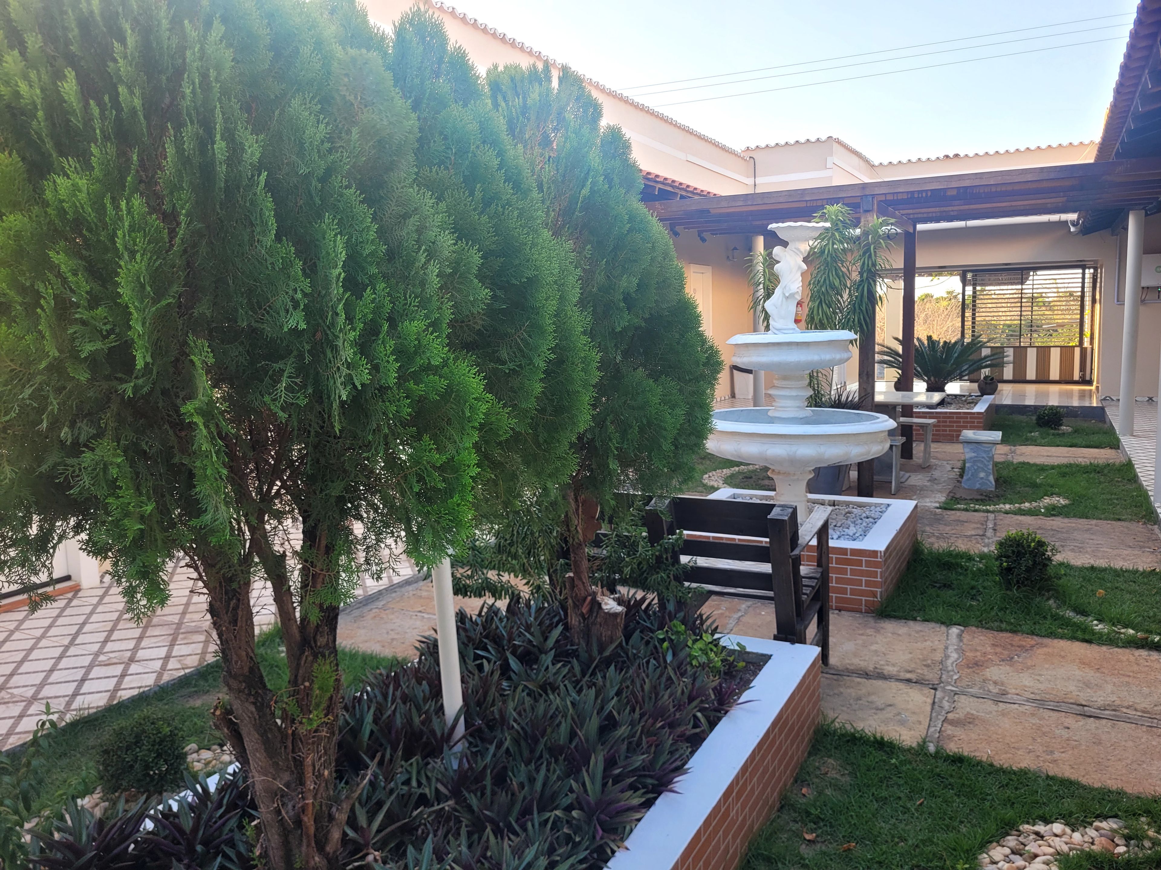 Un jardín ajardinado con una fuente, un árbol y un edificio con techo de tejas.