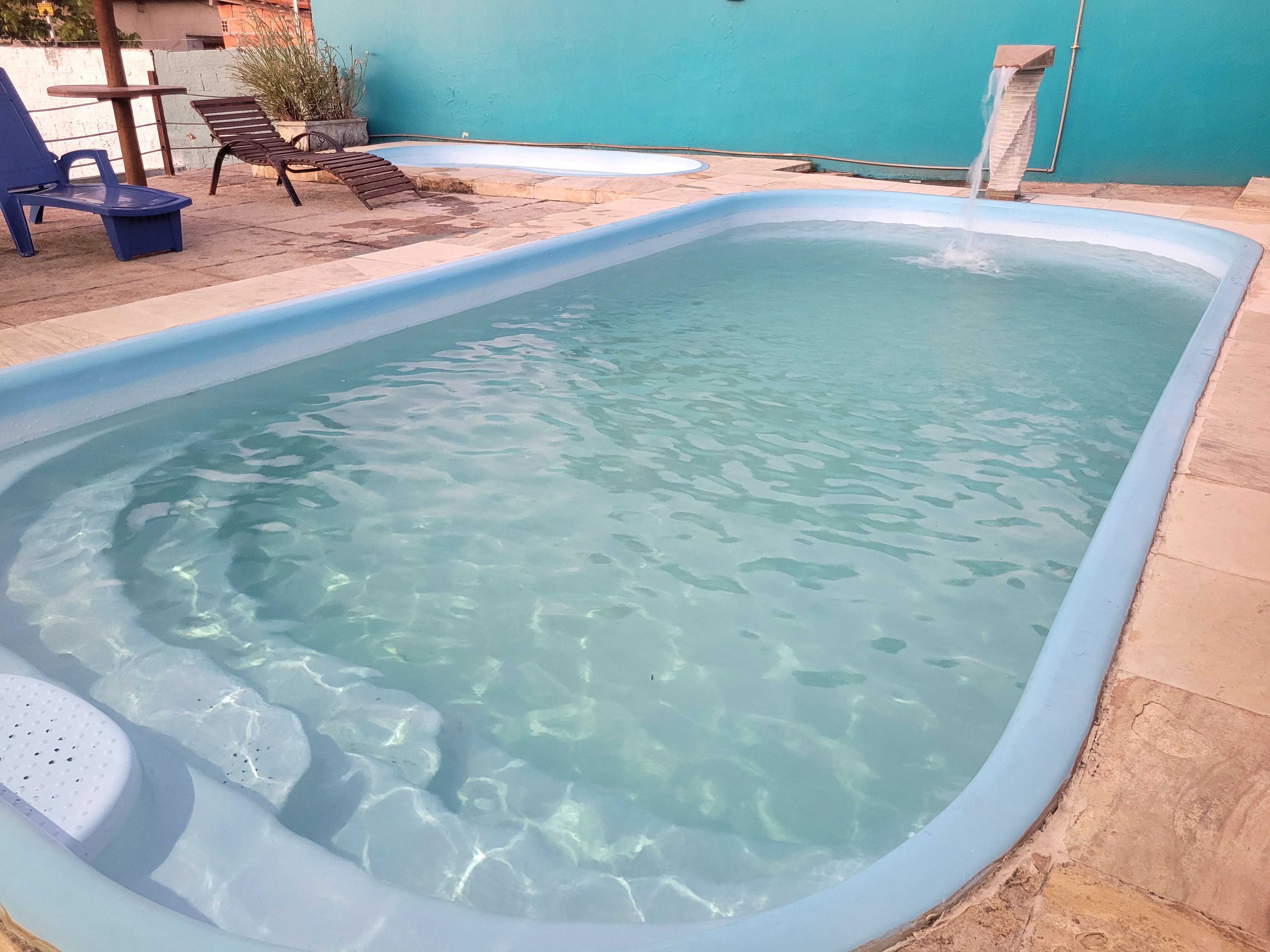 A swimming pool with clear water, surrounded by a tiled patio with lounge chairs and a small table.