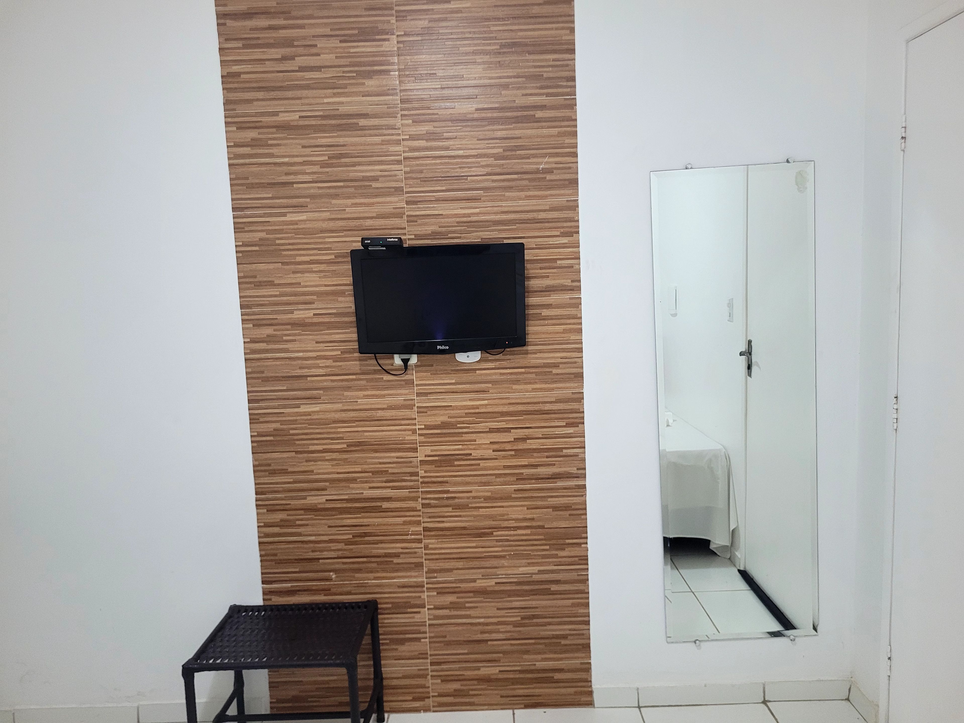 A room with a mounted television, a small table, and a mirror.
