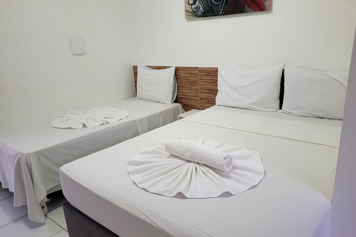 A hotel room with two single beds, each with a neatly folded towel and a pillow.