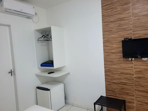 A room with a white wardrobe, a small white refrigerator, a black TV mounted on the wall, and a wooden panel design on the wall. - Pousada Vila Serena (Barreirinhas)
