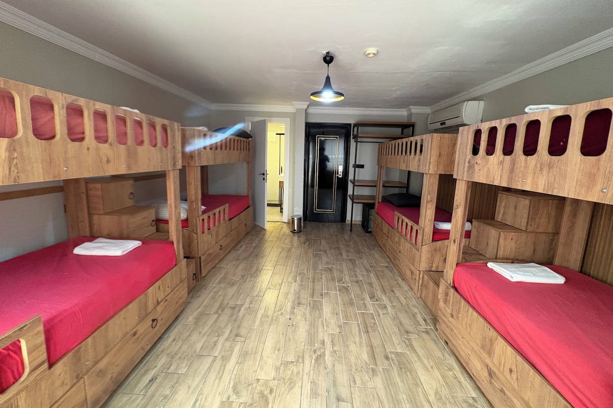 Quarto com beliches, piso de madeira e porta que dá para outro cômodo.