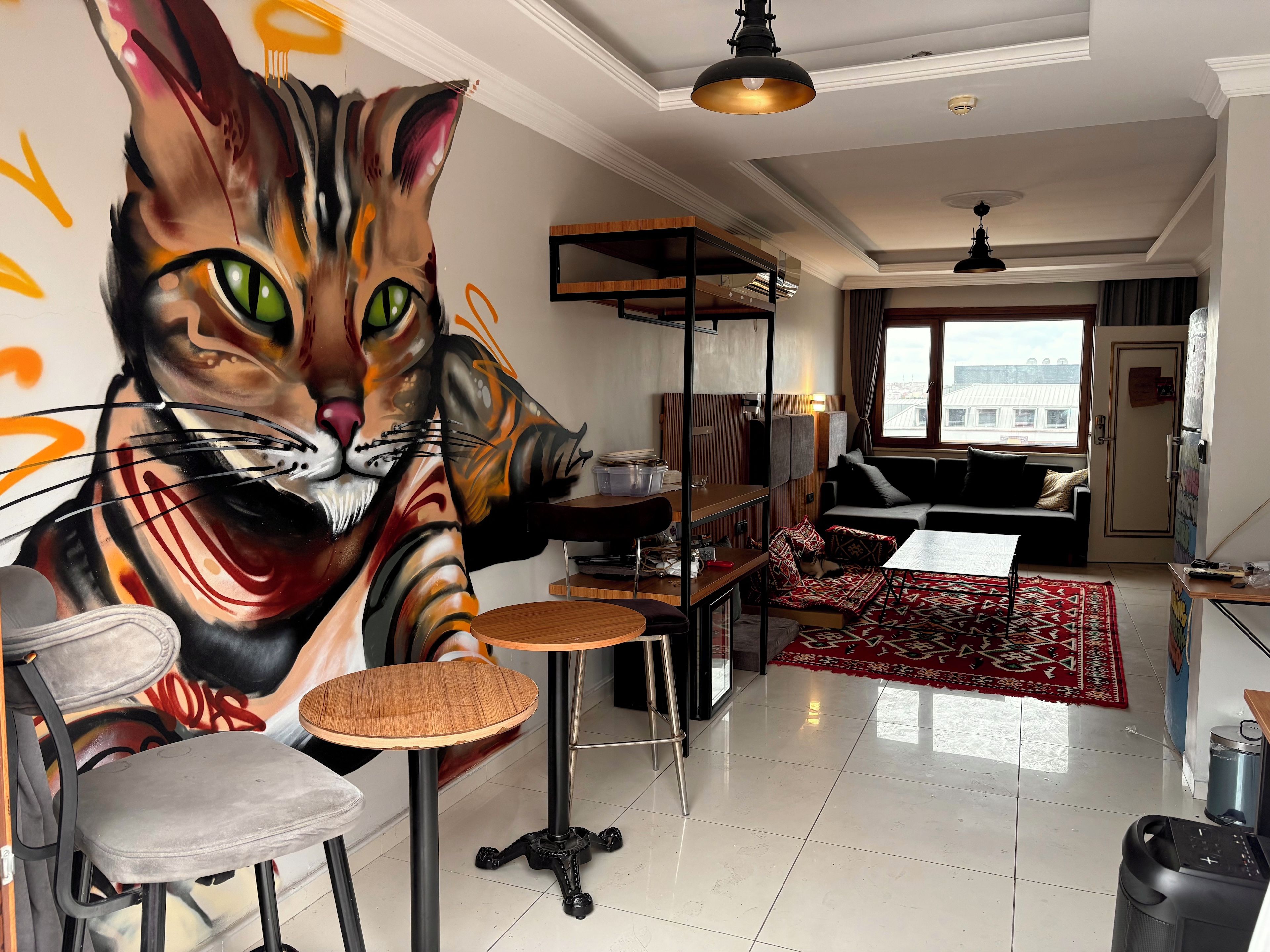 A living room with a large cat mural, a sofa, a dining table, and a kitchen area.