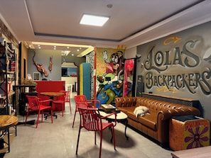 Um ambiente acolhedor com esquema de cores vermelho e marrom, incluindo um sofá, cadeiras vermelhas e um mural com personagens de desenho animado.