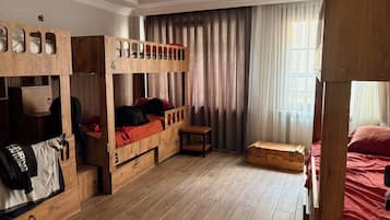 A room with bunk beds, a wooden desk, and a window with curtains.