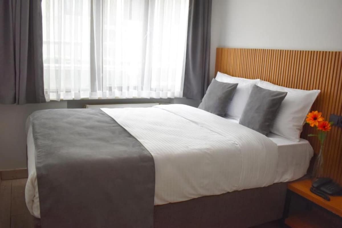 Quarto de hotel com cama, mesa de cabeceira com telefone e janela com cortinas.