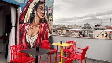 Eine Dachterrasse mit roten Stühlen, einem gelben Tisch und einem Wandbild einer Frau.