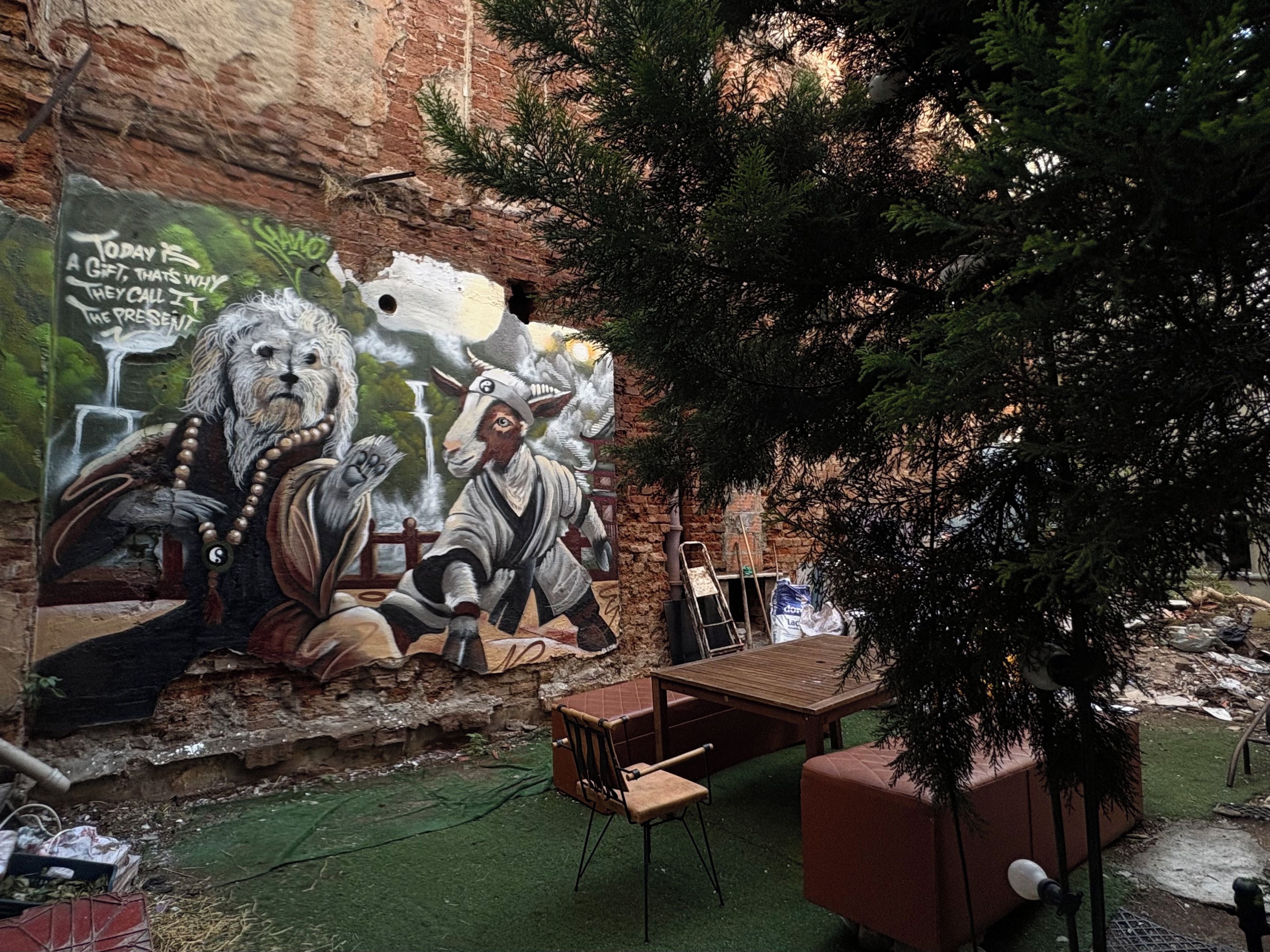 A mural with a lion and a figure, outdoor seating, and a brick wall.