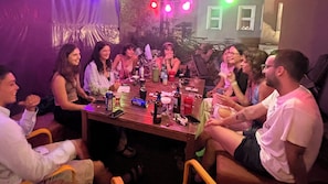 Um grupo de pessoas sentado em volta de uma mesa com garrafas e latas, indicando um encontro social.