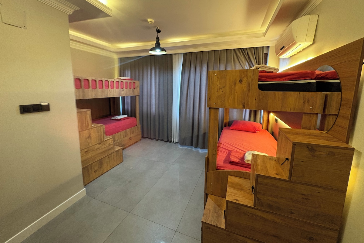 Quarto com beliches, ventilador de teto e janela com cortinas.