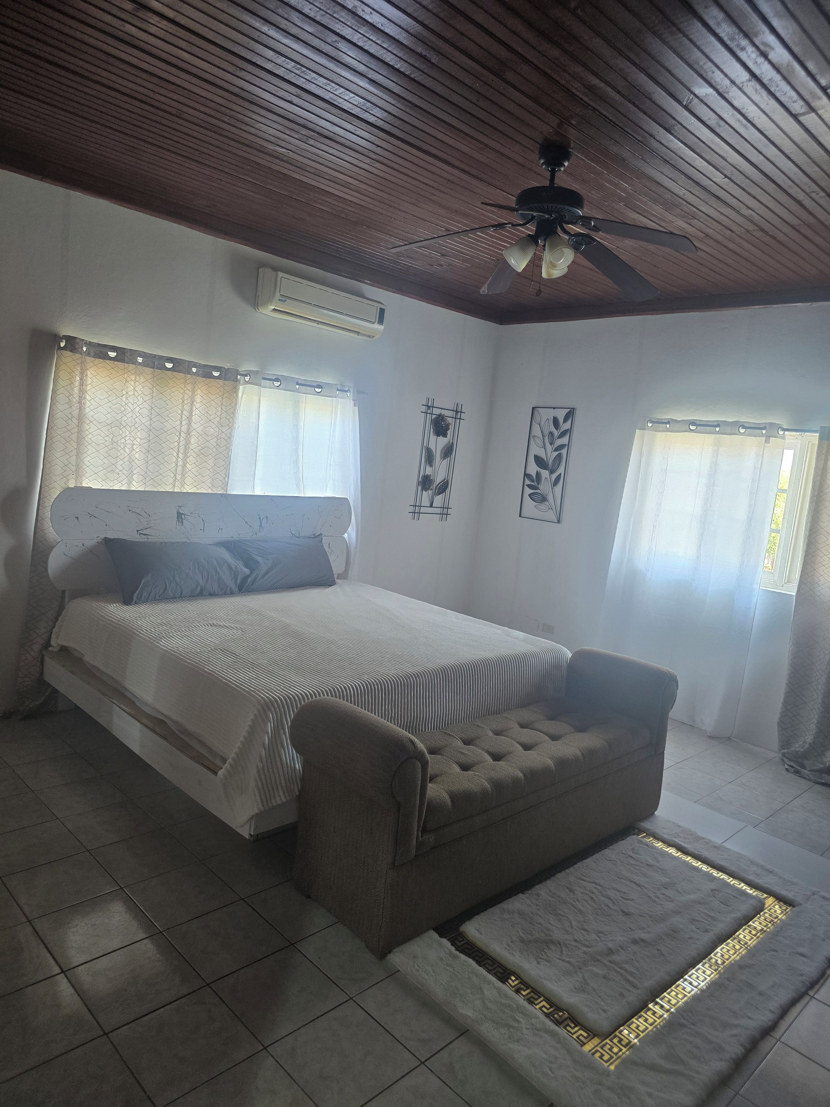 A bedroom with a bed, a sofa, a ceiling fan, and a window with curtains.