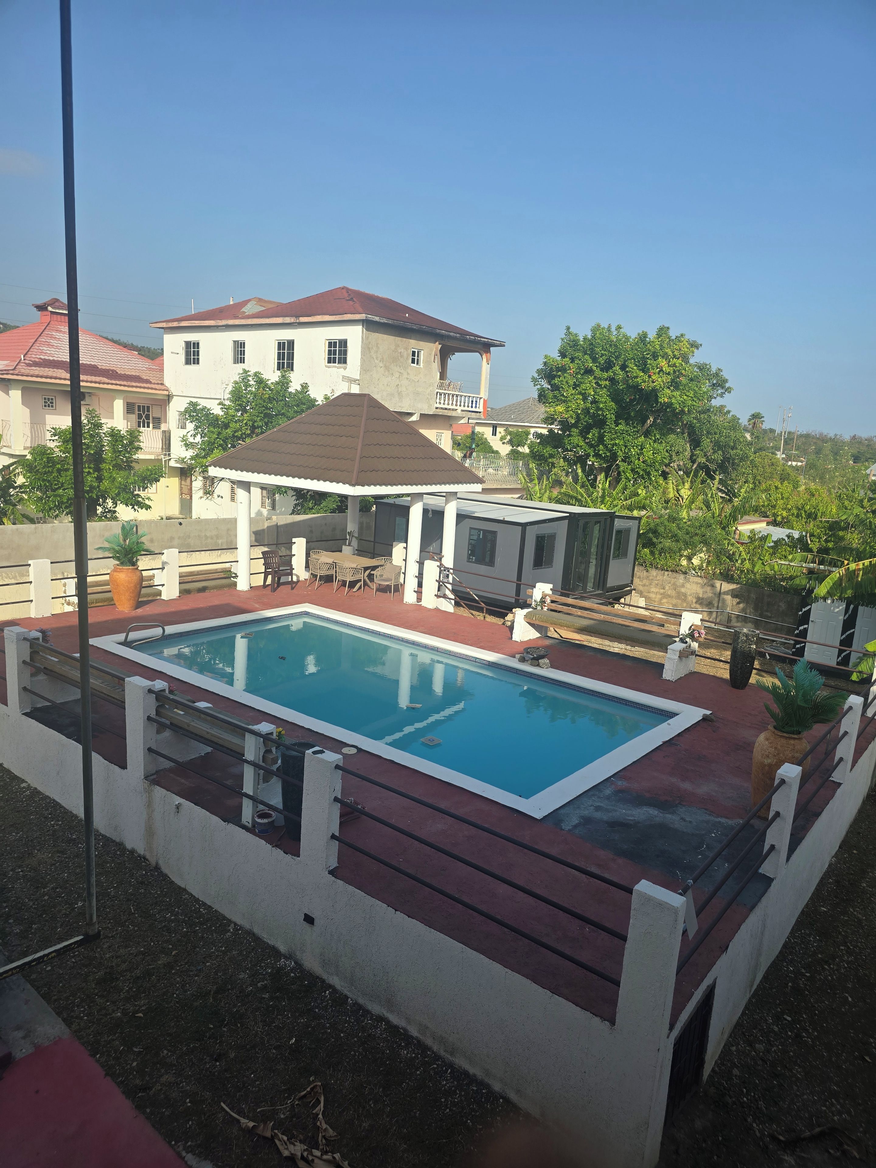 A swimming pool with a patio area, surrounded by a fence, and a house in the background.