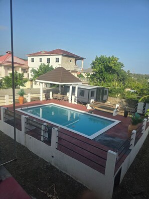 Ein Schwimmbecken mit einer Terrassenanlage, umgeben von einem Zaun, und ein Haus im Hintergrund.