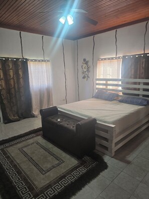 Ein Schlafzimmer mit einem Bett, einer Bank, einem Deckenventilator und Vorhängen.