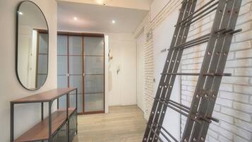 A hallway with a wooden bench, a mirrored wall, a sliding glass door, and a metal ladder leaning against a brick wall.