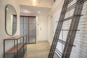 Um corredor com um banco de madeira, parede espelhada, porta de vidro deslizante e uma escada de metal encostada em uma parede de tijolos.