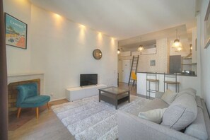 A living room with a sofa, a television, a coffee table, and a fireplace. There is a kitchen area with a brick wall and a ladder. - Bright 1-bedroom apartment Apartment with an elevator, air conditioning, and Wi-Fi (Cannes)