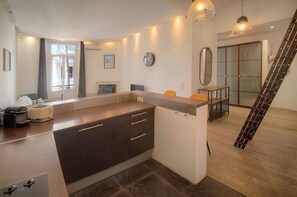 Et moderne køkken med en central ø, et spiseområde med bord og stole, samt en trappe til en etage ovenpå.