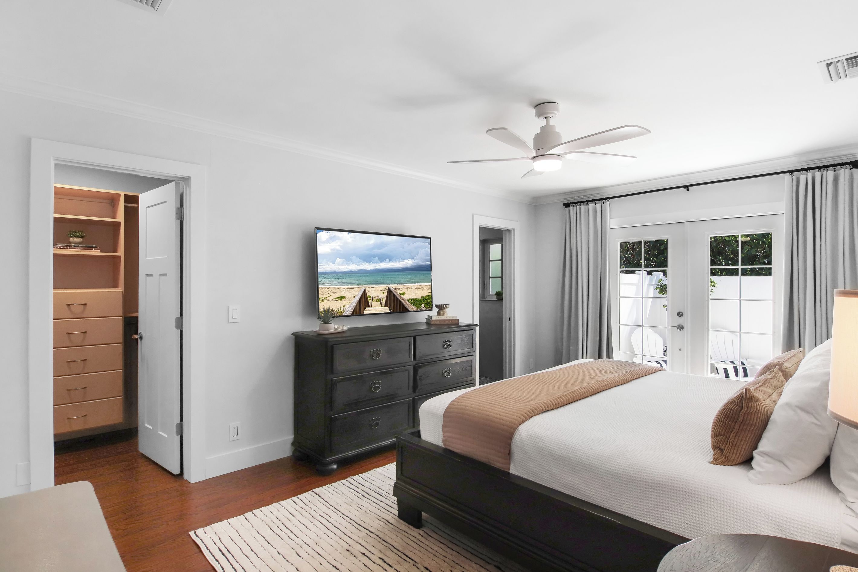 Une chambre à coucher comprenant un lit, une commode, un téléviseur et un ventilateur de plafond.