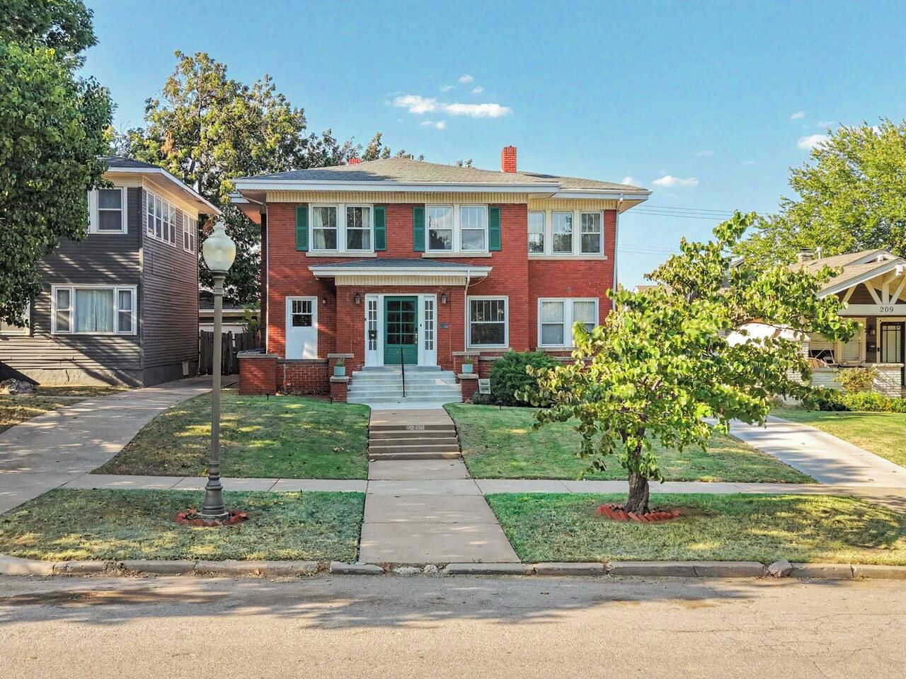 A two-story residential building with a front entrance, a small front yard, and a street view.