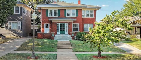 A two-story residential building with a front entrance, a small front yard, and a street view.