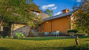 Une maison en bois à l’allure rustique, dotée d’un mur en pierre, d’un patio couvert avec des chaises et d’un jardin.