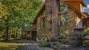 A stone building with a wooden deck, outdoor seating, and a basketball hoop. - NEW! Alpine Lodge | Large Home on 5 Acres | Near Alpine Camp & DeSoto State Park (Mentone)