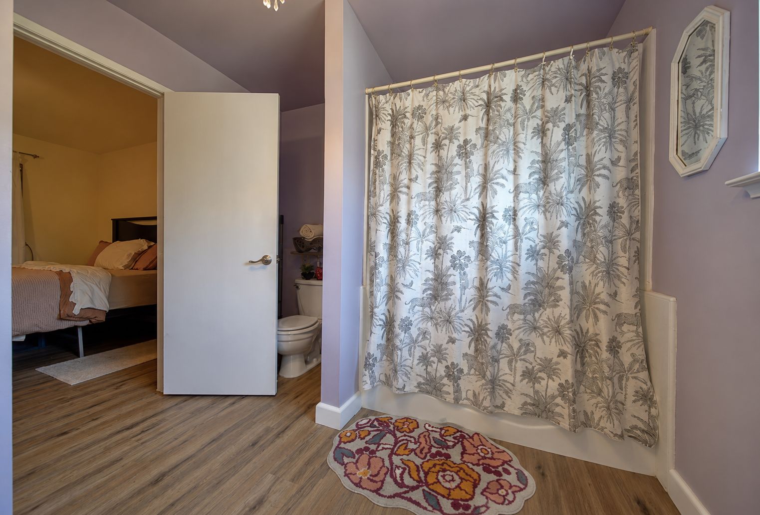 A bedroom with a bed, a door leading to a bathroom, and a shower curtain with a floral pattern.