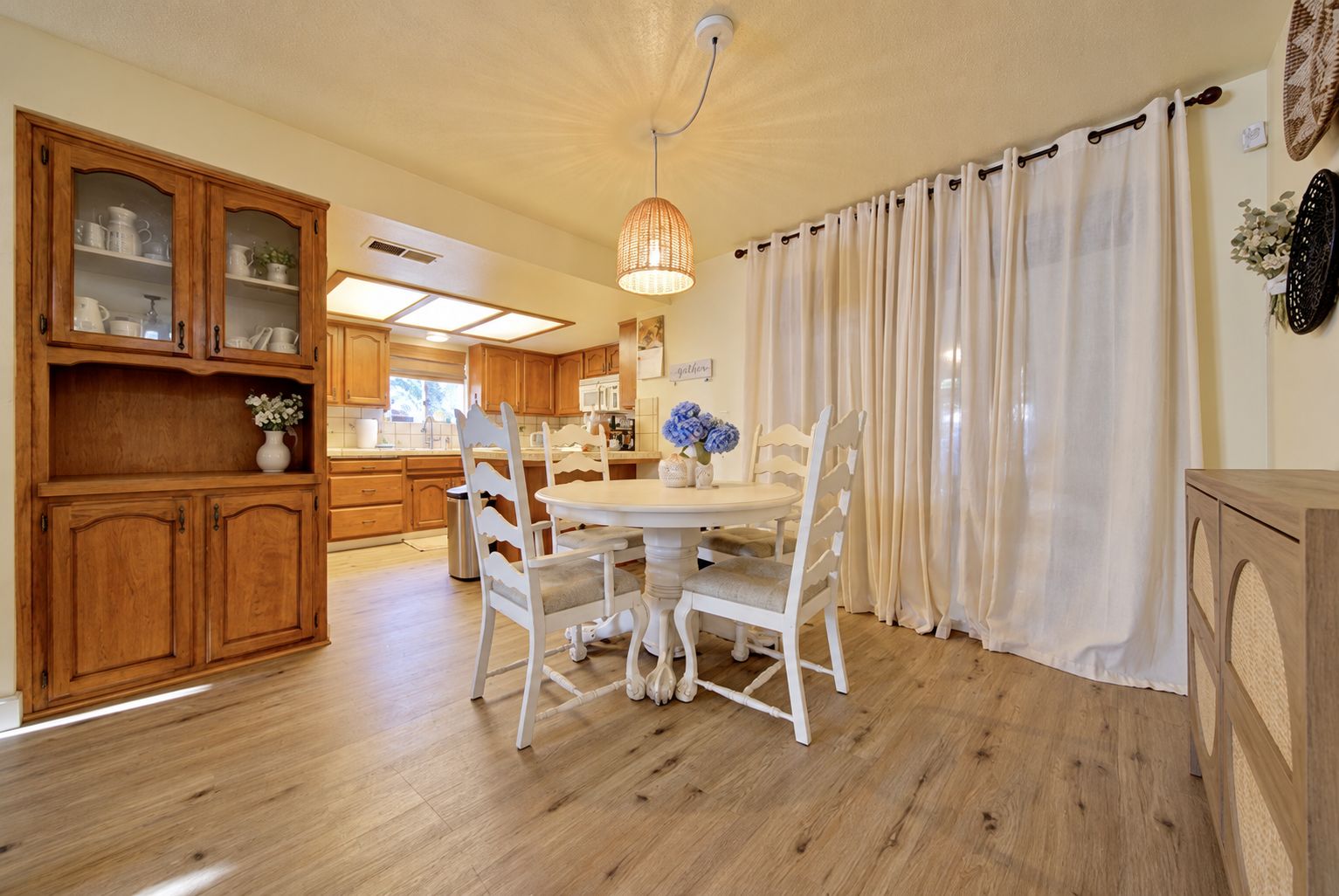 A kitchen with wooden cabinets, a dining table with white chairs, and a hanging light fixture.