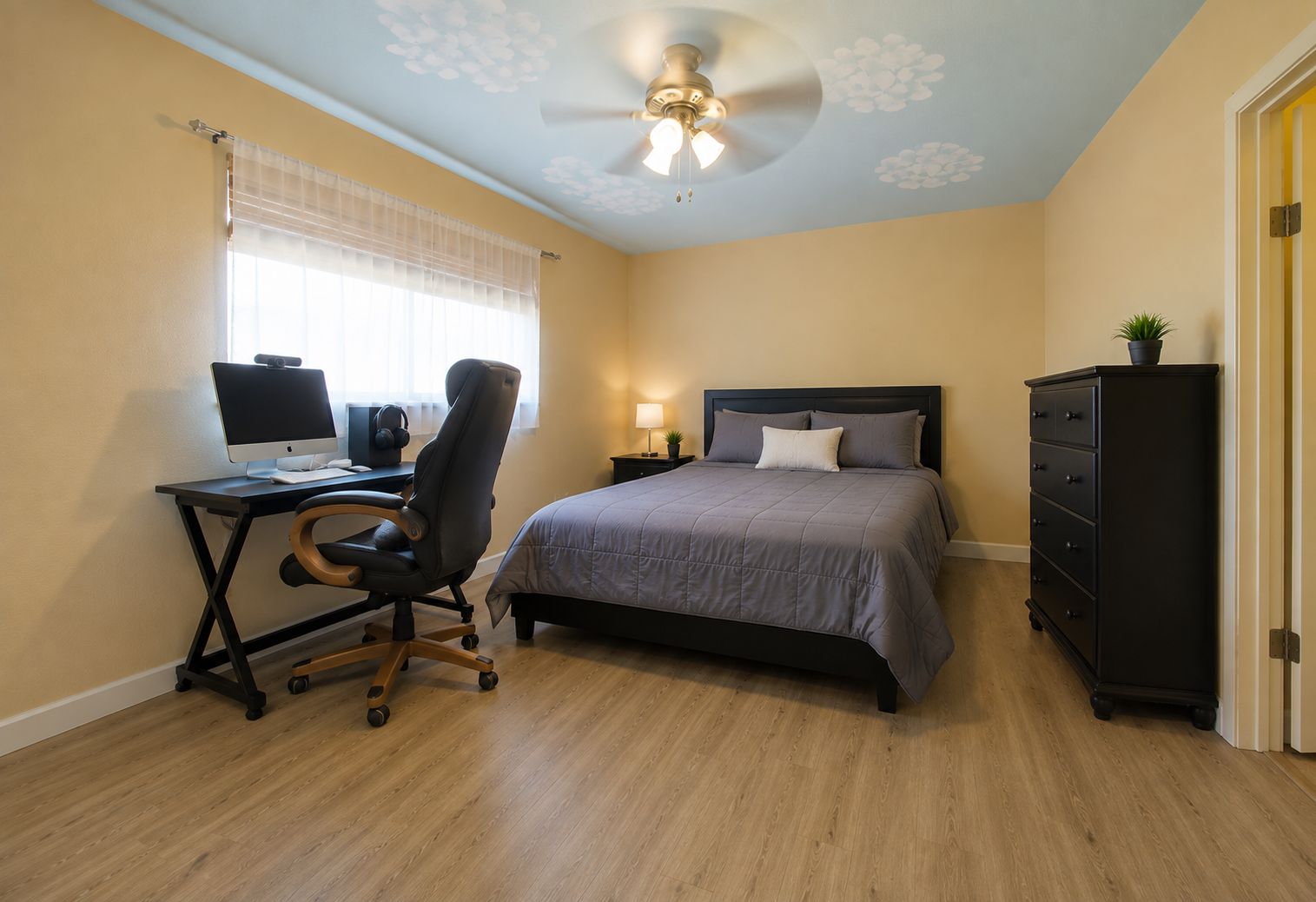 Un dormitorio con cama, escritorio, silla, ventilador de techo y cómoda.
