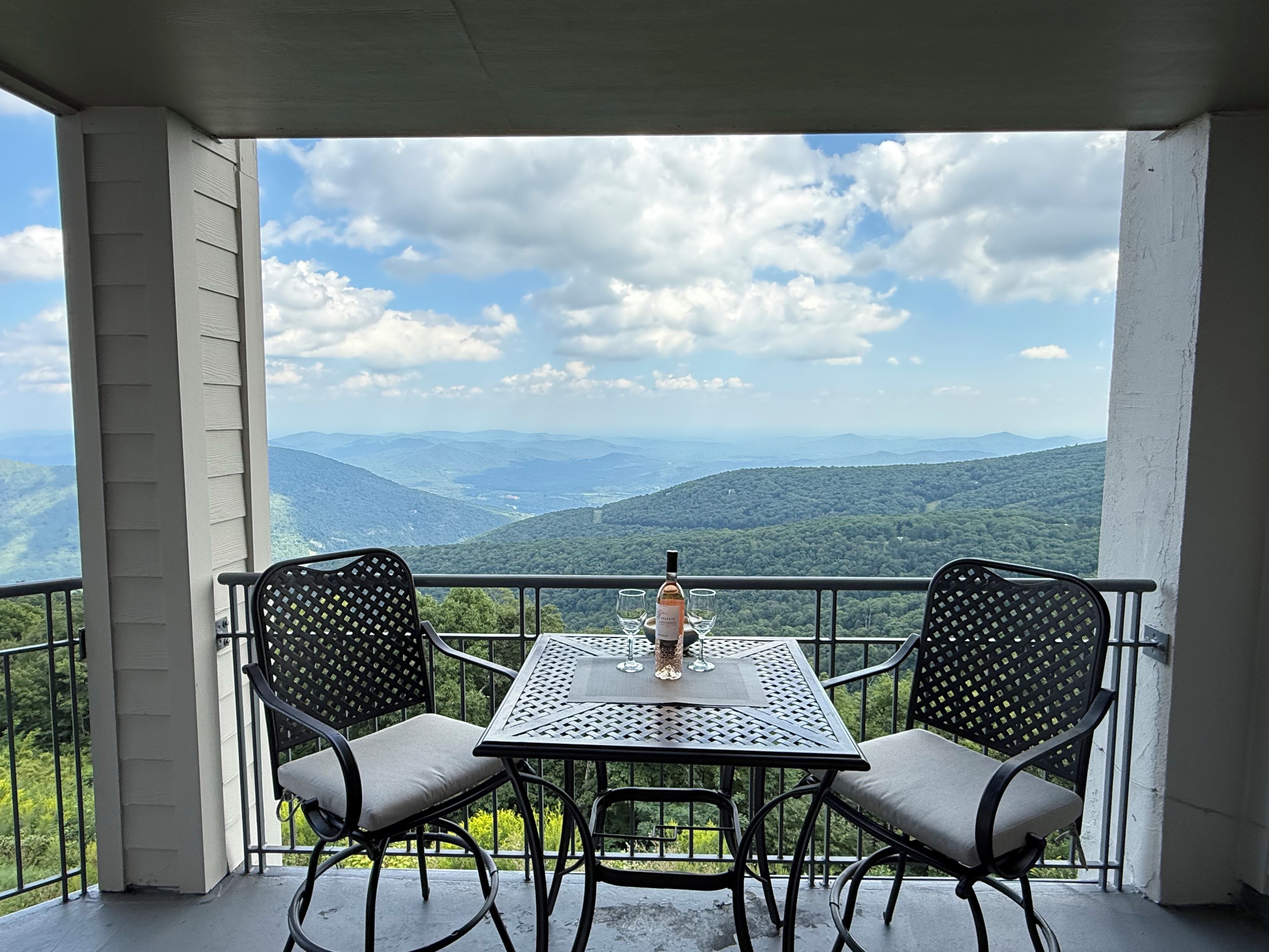 A balcony with two chairs and a table, overlooking a mountainous landscape.