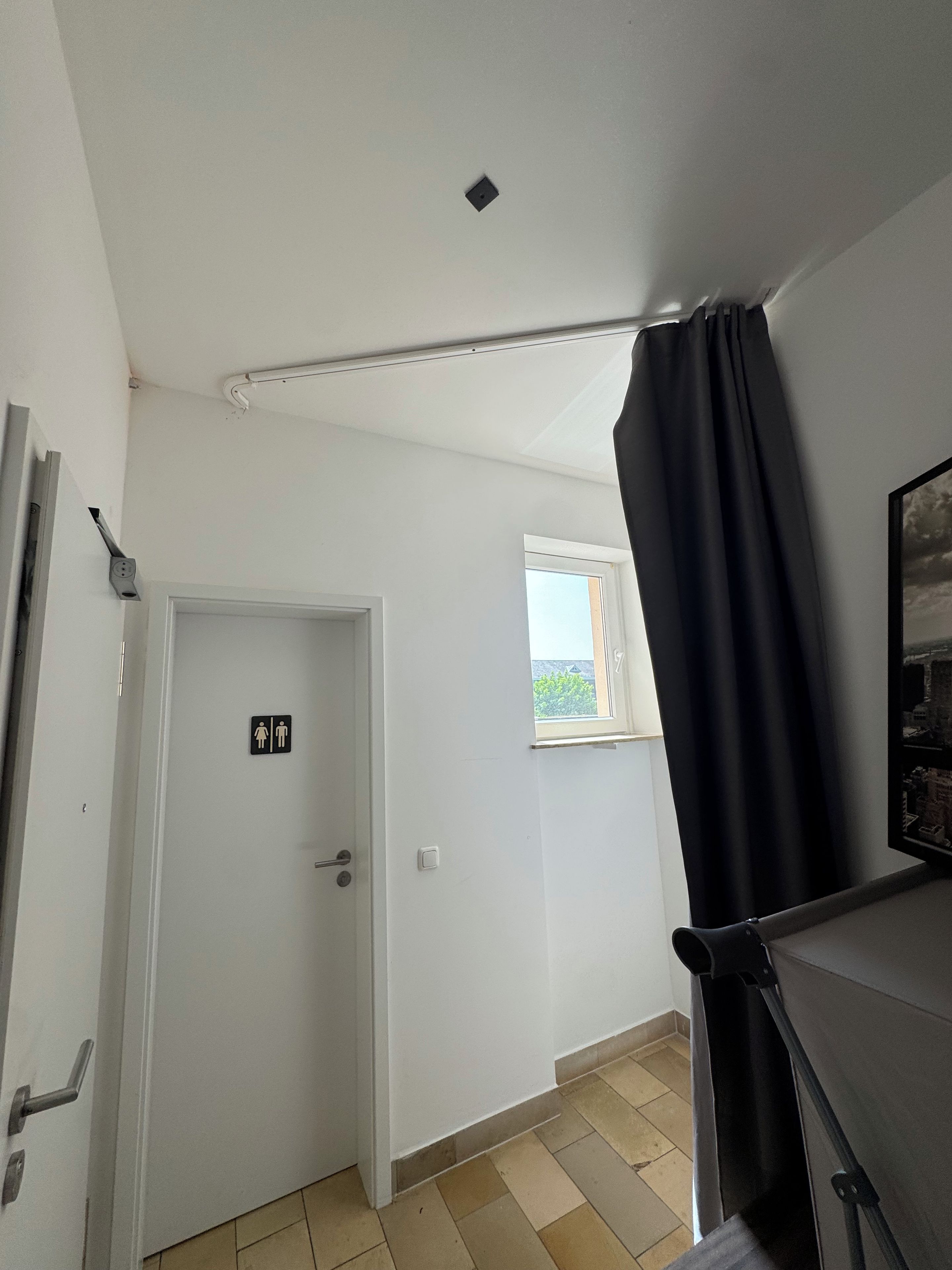 Ein Zimmer mit Tür, Fenster, Vorhang und Blick ins Freie.