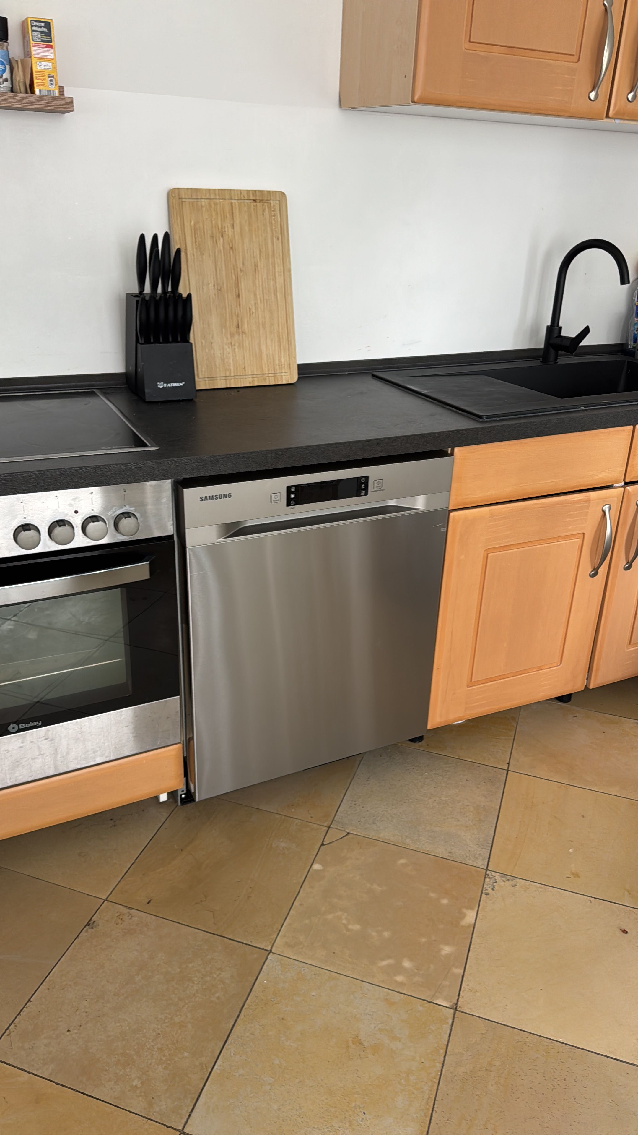 A kitchen with a built-in oven, dishwasher, and a black faucet.