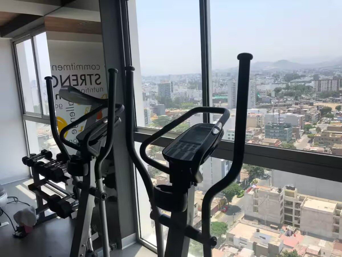 Ein Fitnessstudio mit Trainingsgeräten und einem großen Fenster mit Blick auf eine Stadtlandschaft.
