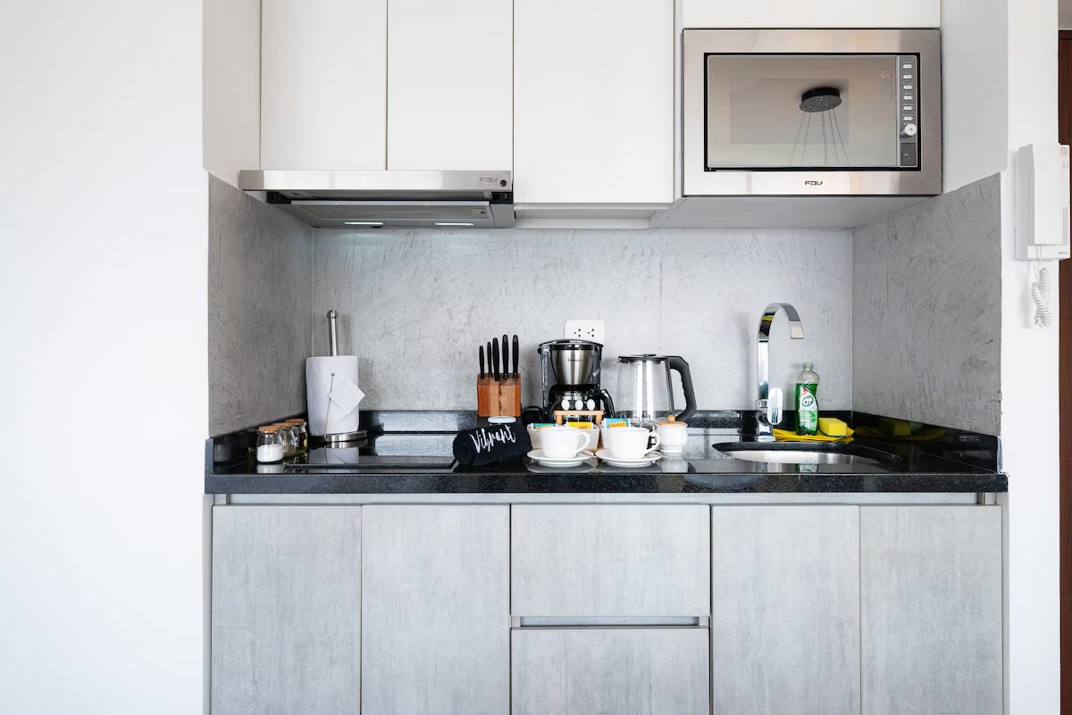 Cocina compacta con microondas, cafetera y utensilios sobre la encimera.