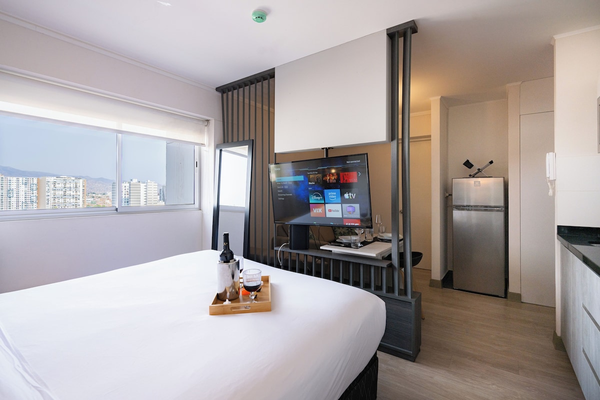 Ein Hotelzimmer mit Bett, Fernseher, Minibar und Blick auf die Stadt.